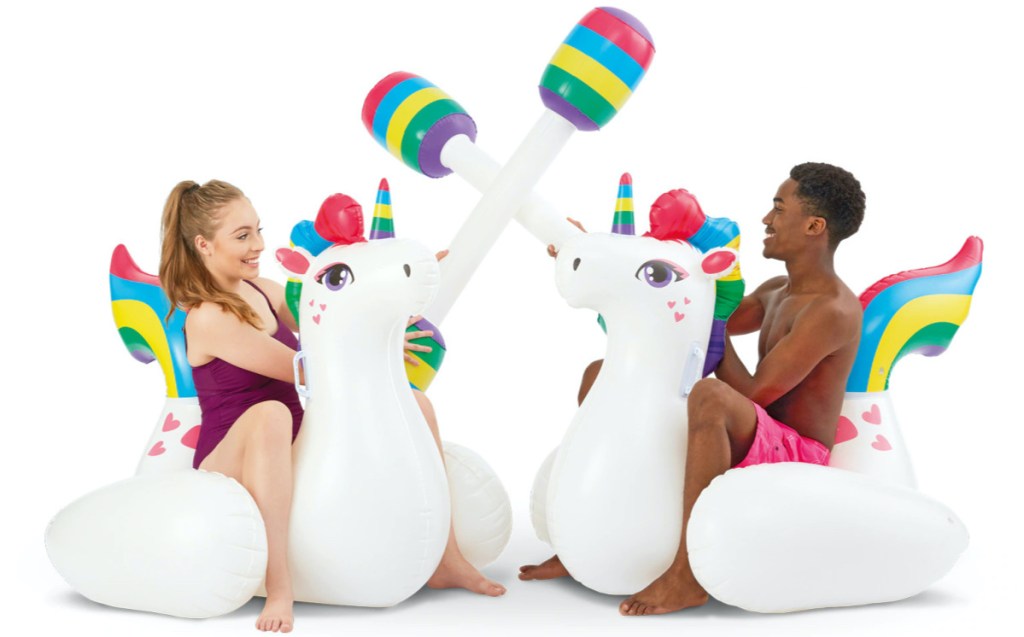 girl in purple bathing suit and boy on pool float unicorns with inflatable jousting sticks