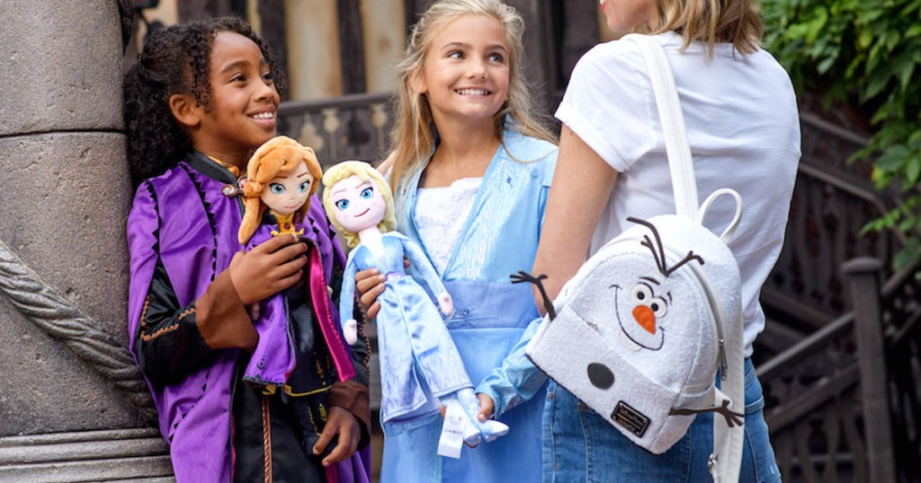 two girls holding disney frozen plush dolls and woman wearing a white olaf mini backpack on one shoulder