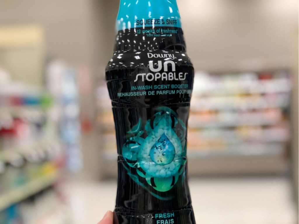 person holding up a black and blue bottle of downy unstopables scent booster beads