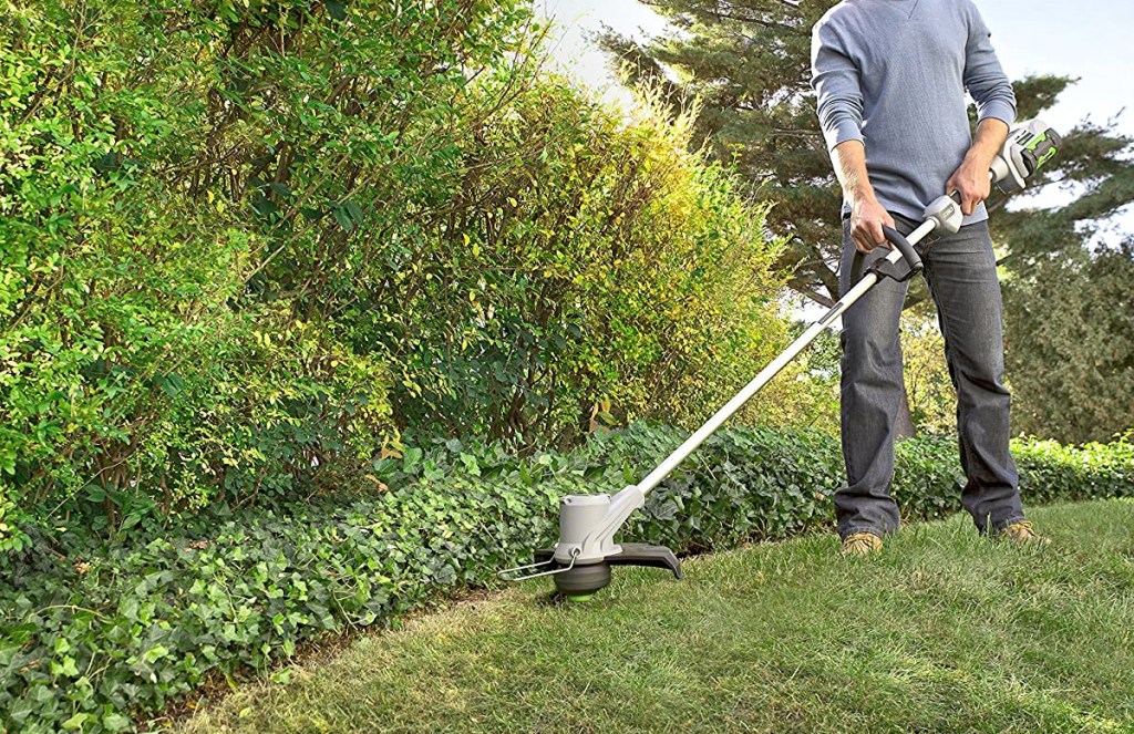 man using a grey cordless trimmer to edge lawn next to garden
