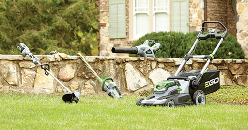 variety of lawn power tools sitting on grass next to stone wall