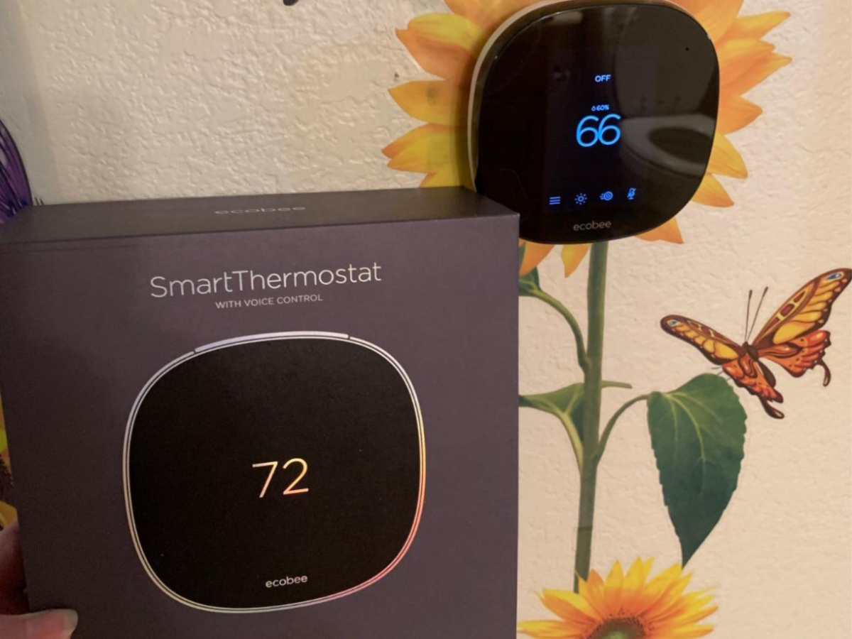 ecobee smart thermostat with sunflower designs on the wall and woman holding box