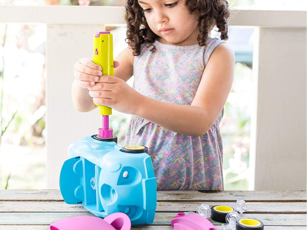 little girl using pretend drill on blue toy car