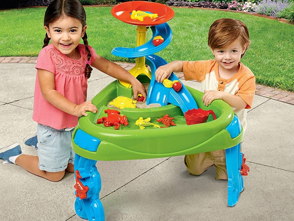 two children playing with water and sand play table outside