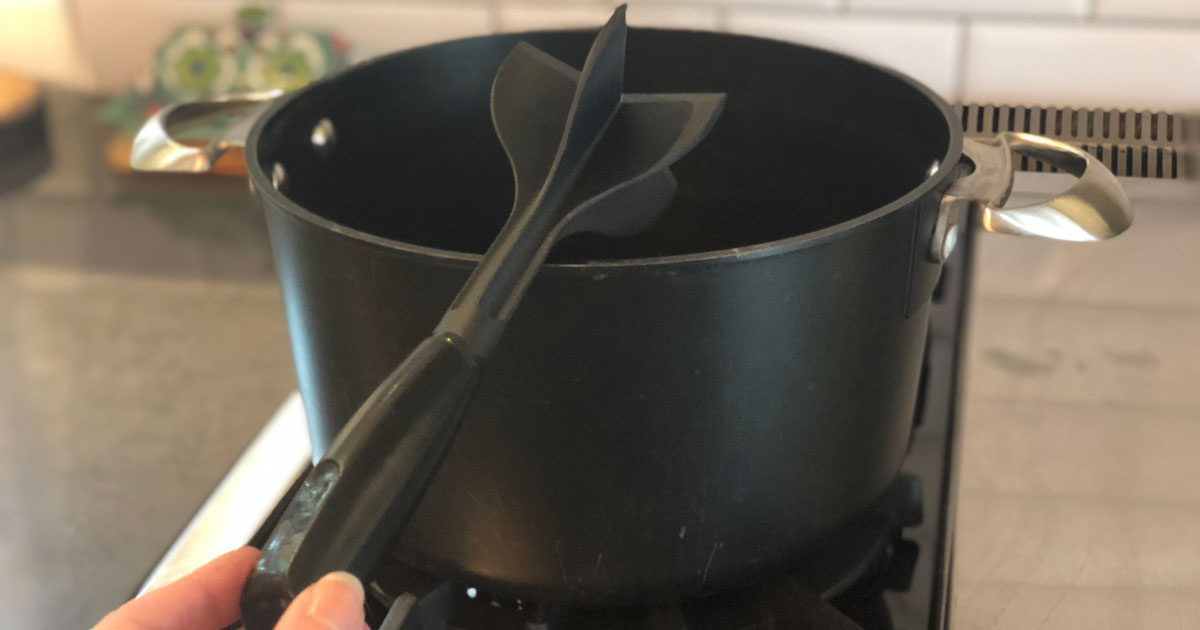 hand holding black meat chopper over large black pot in kitchen