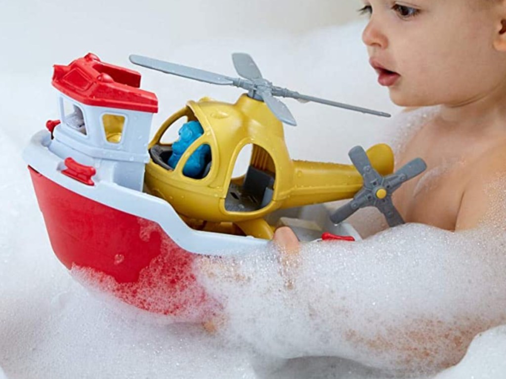 young boy playing with toy rescue boat in bath with lots of bubbles