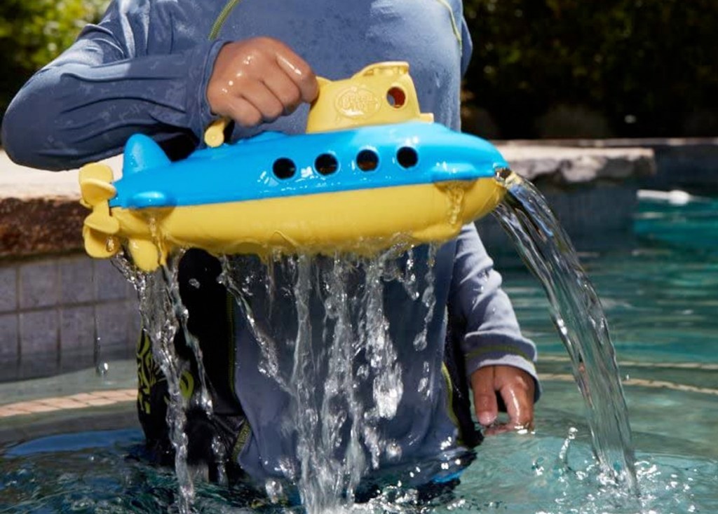child pulling a blue and yellow submarine toy out of water in a pool