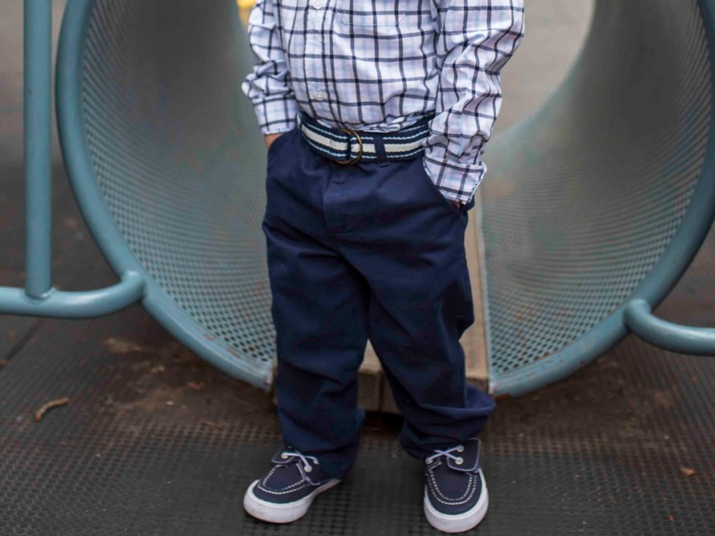 young boy in casual sneakers, dark blue chino pants with belt, and blue and white button up long-sleeve top