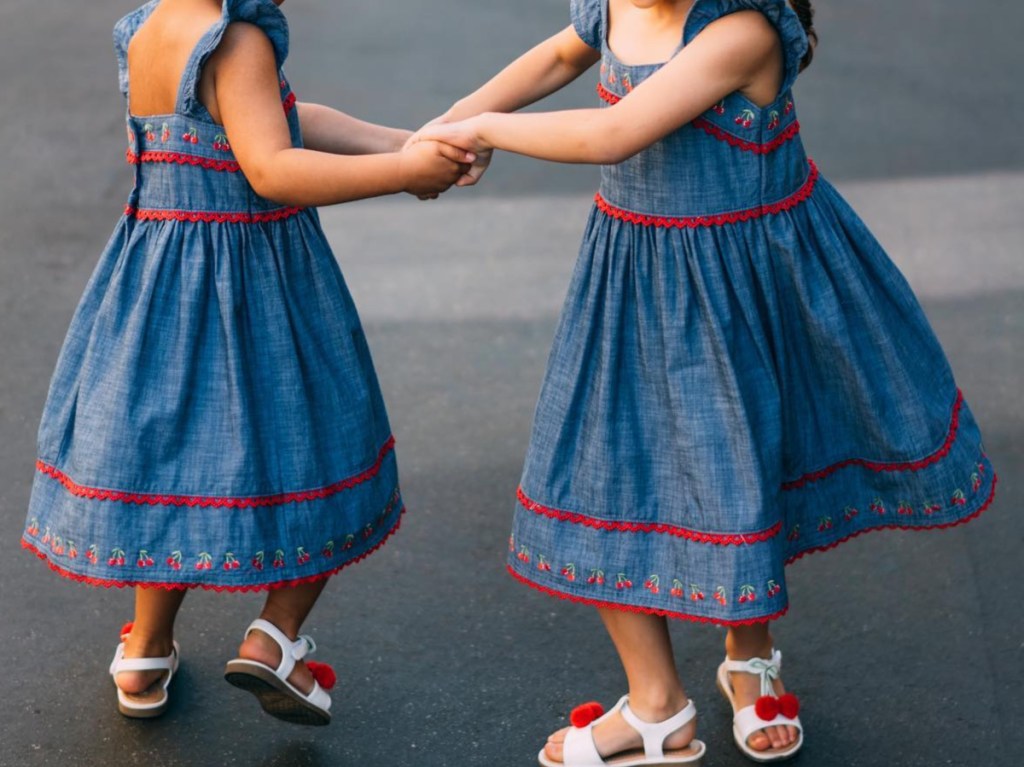 two girls holding hands spinning around in blue dresses with embroidered cherries