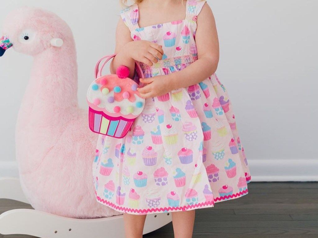 young girl holding cupcake bag in pink and white cupcake printed dress