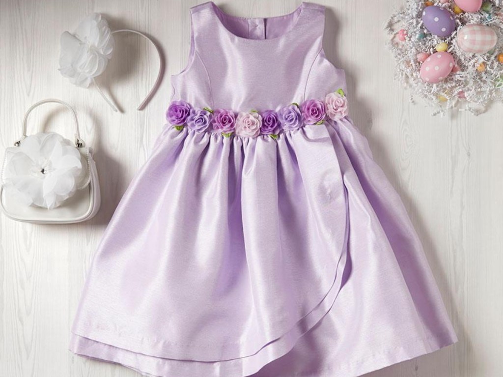 girls purple dress with purple applique flowers at waist laid out next to white headband and purse