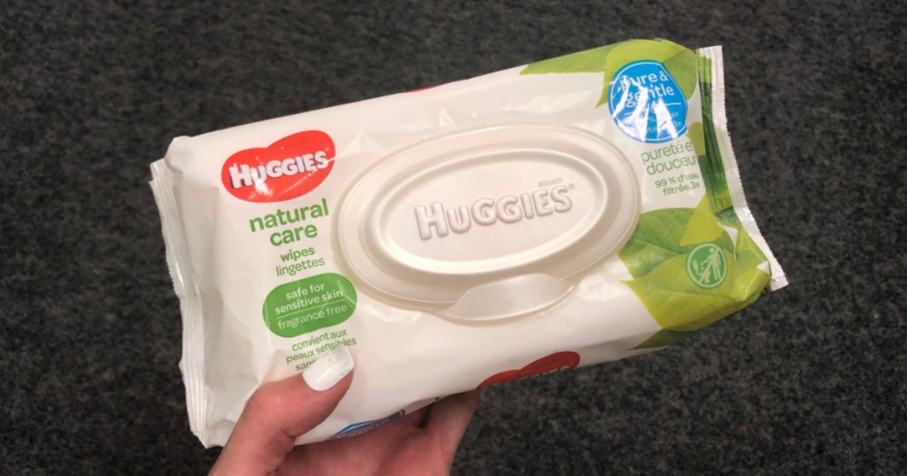 manicured hand holding pack of baby wipes in store aisle