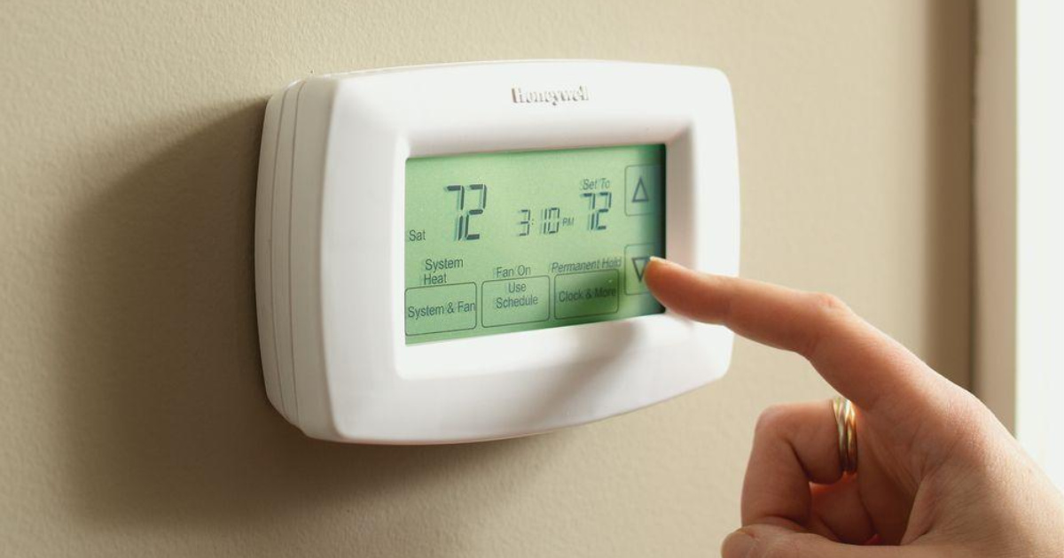 Finger pushing screen to change ac temperature on thermostat for lower electric bill