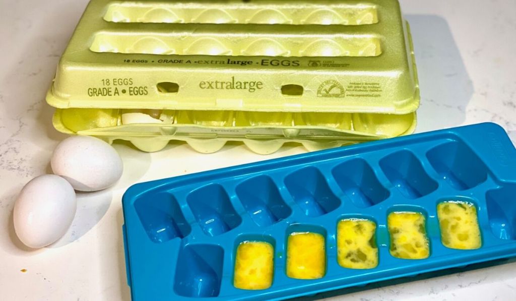 Whisked eggs in an ice cube tray next to egg carton and two eggs on the counter