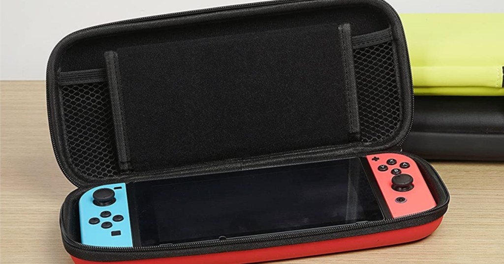 handheld gaming console in black and red case on wood table with yellow case and black case stacked behind it