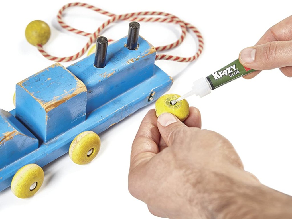 hands putting krazy glue on wheel of broken toy train
