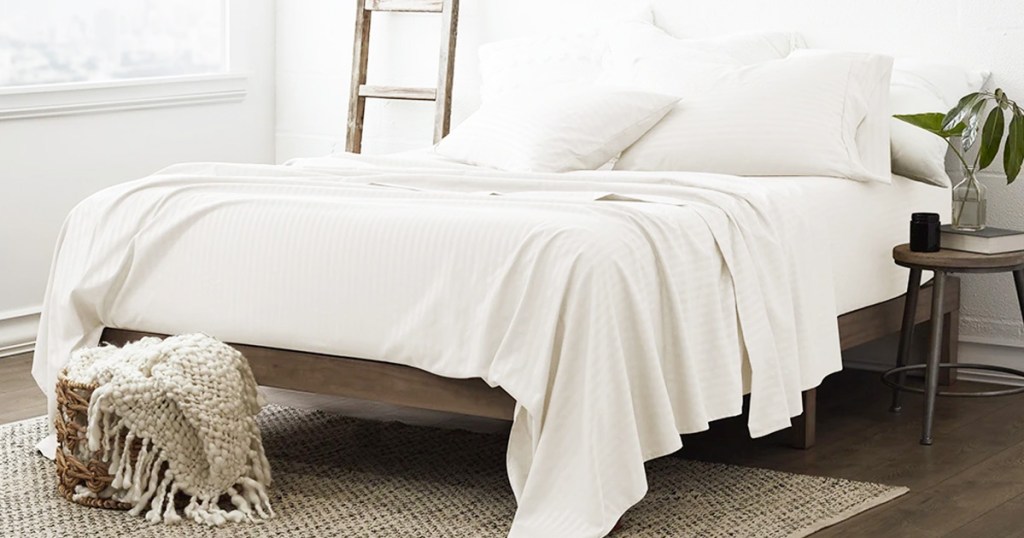 white sheet set on bed with basket of throw blankets at foot of bed