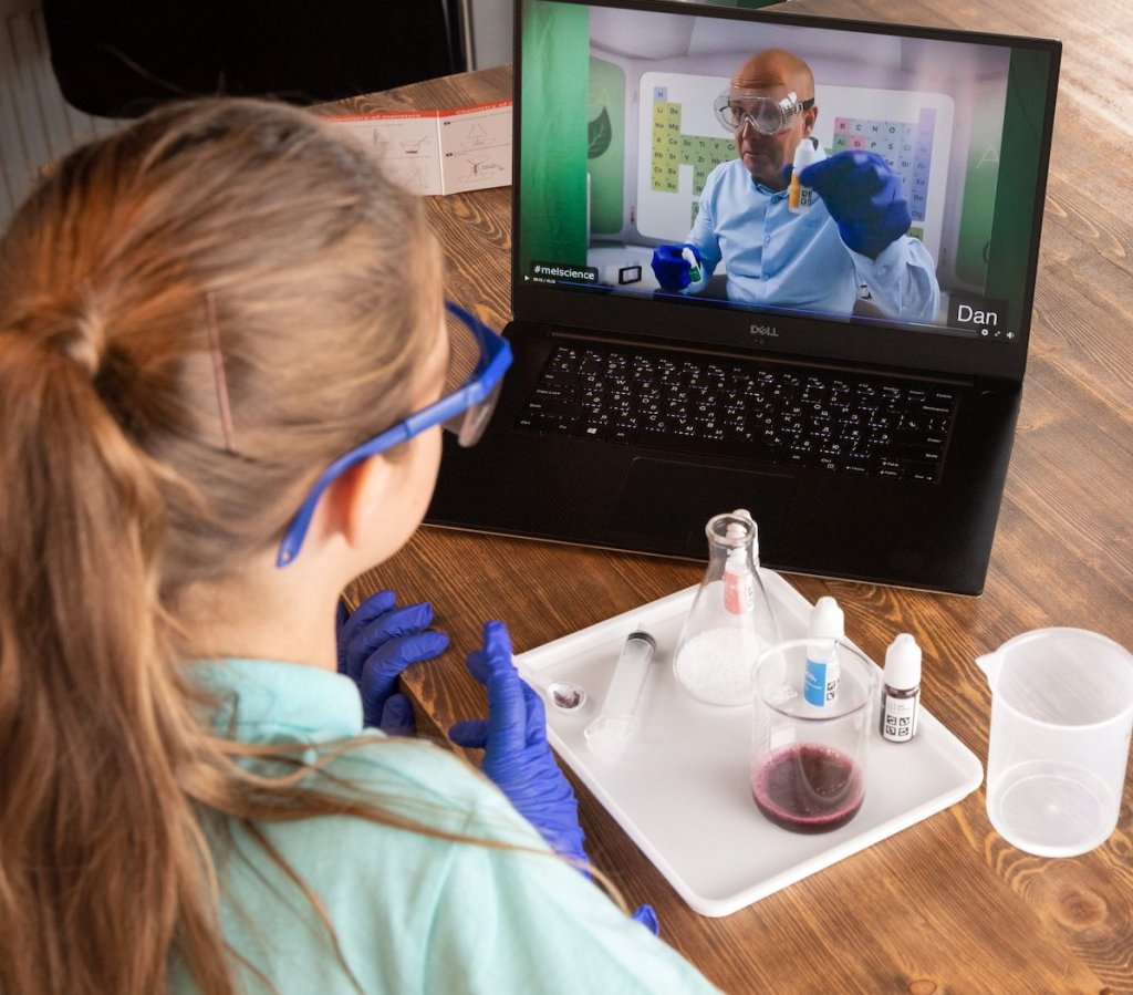 girl sitting at table with laptop and science experiment