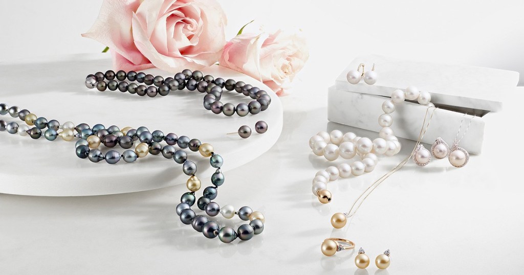 pearl necklaces, bracelets, and earrings on white display with pink roses in background