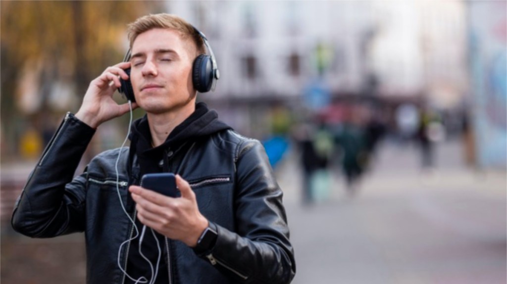 man with headphones on holding phone with blurred city street in background