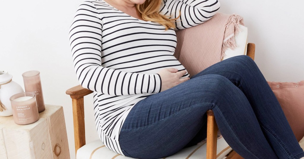pregnant woman sitting in chair with hand on baby bump wearing striped top and jeans