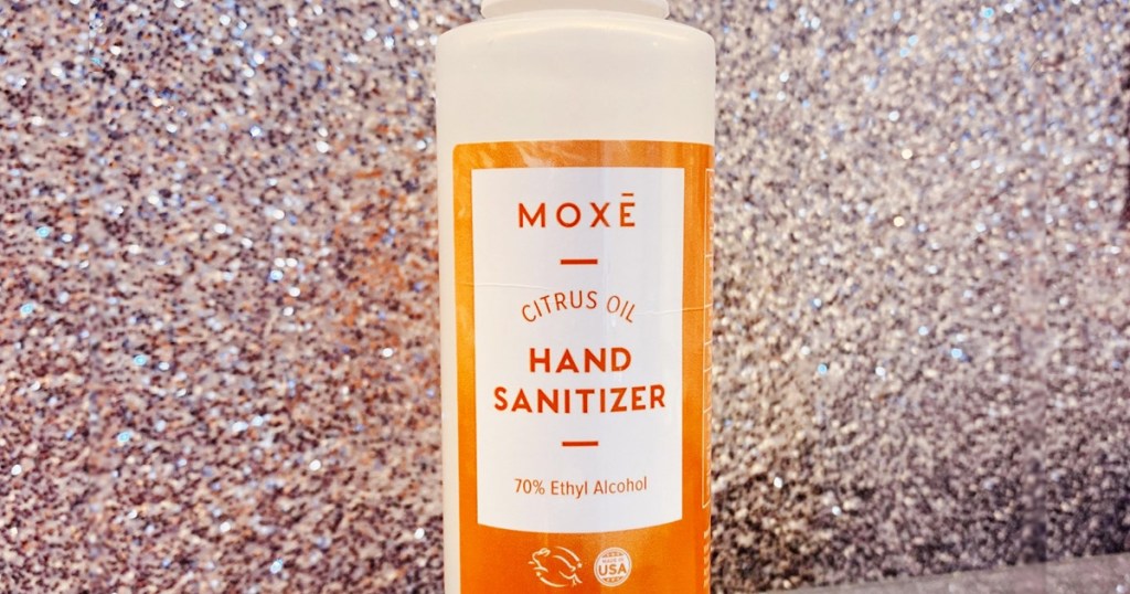 bottle of moxe brand hand sanitizer with orange label against glitter wall