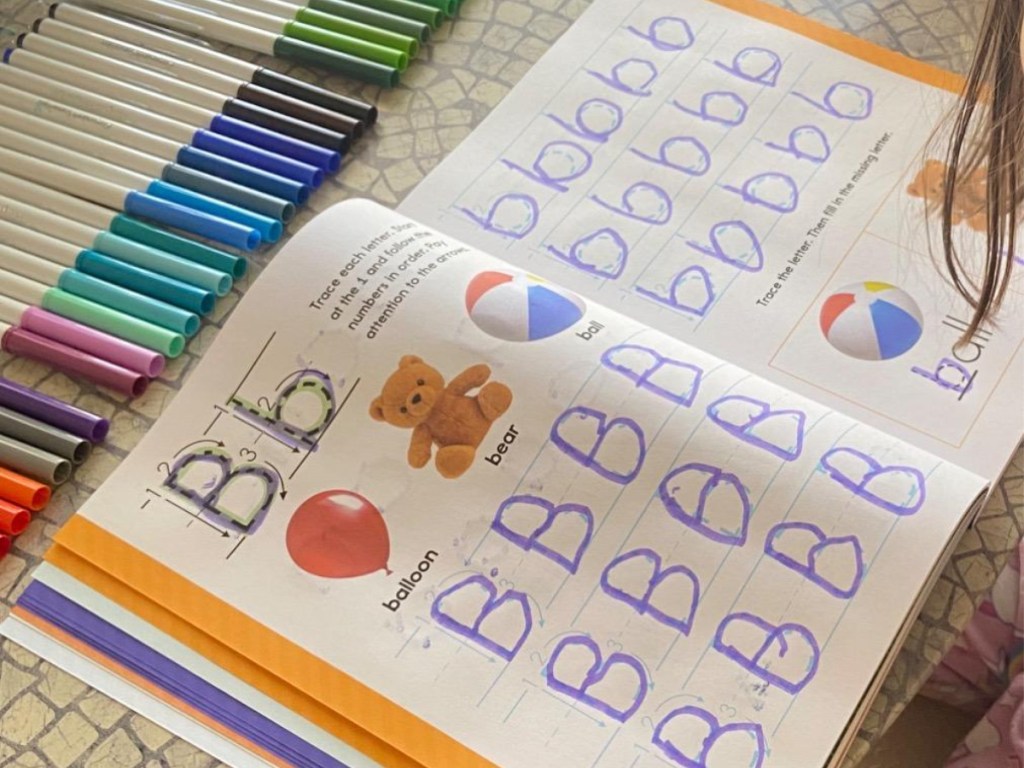 child using learn-to-write book on table with colored markers