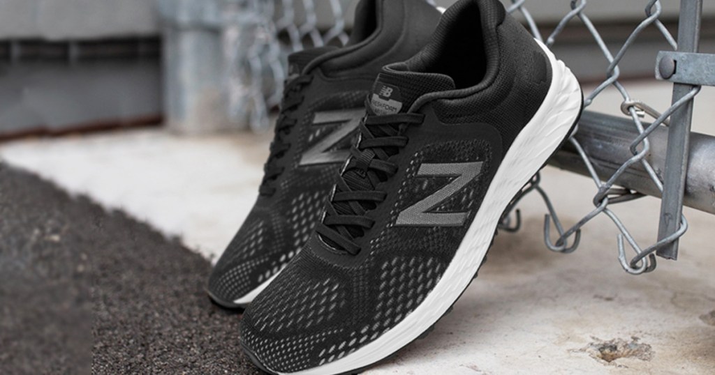 pair of black mesh new balance shoes leaning up against chain link fence