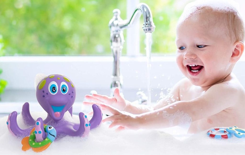 baby in bath in sink playing with purple octopus toy