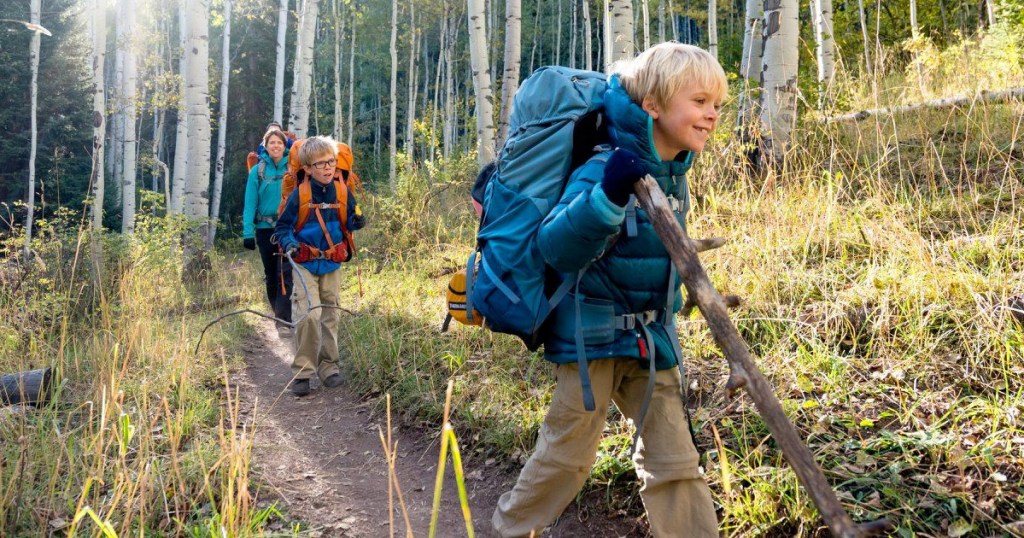 blonde child backpacking through woods with teal backpack