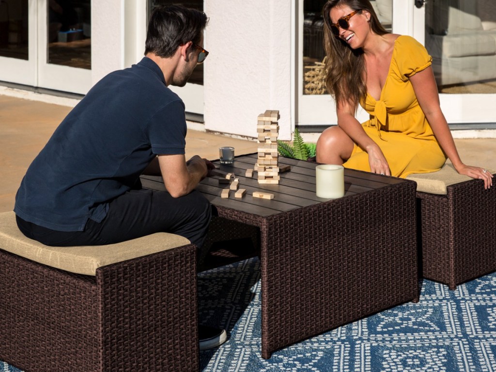man and woman sitting on brown wicker patio furniture playing Jenga