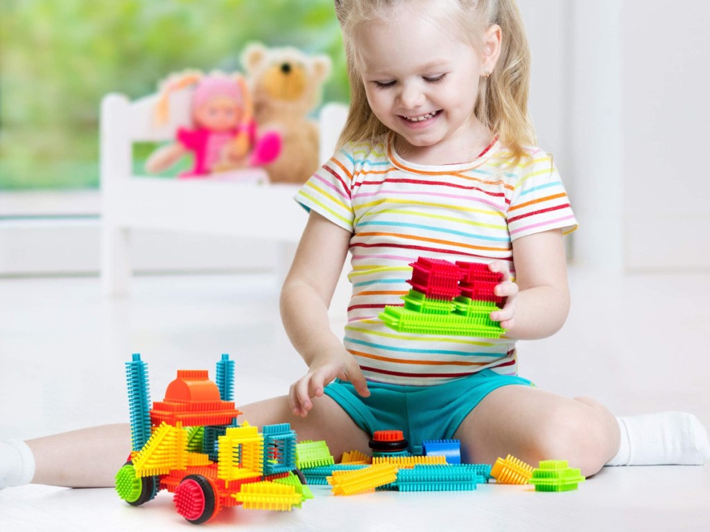 little girl sitting on the floor playing with bristle blocks