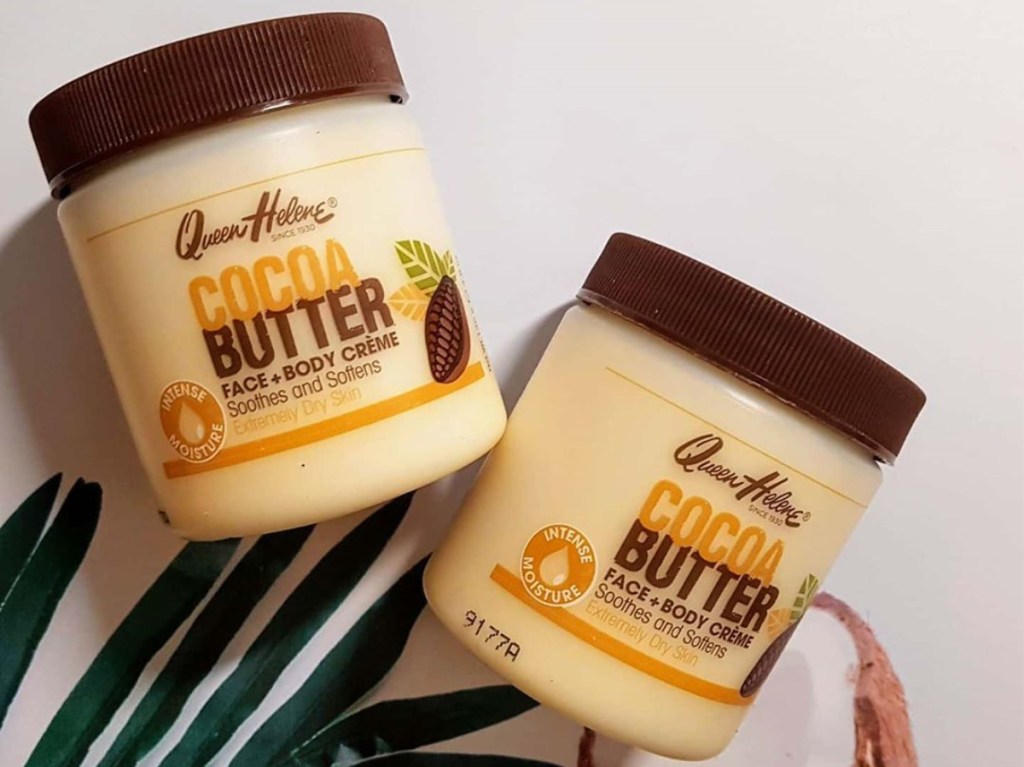 two tubs of cocoa butter lotion on white background with green palm leaf