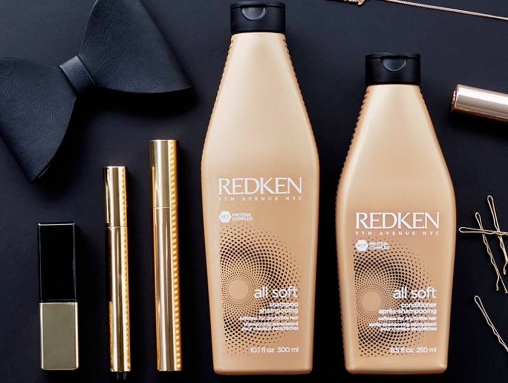 gold bottles of redken shampoo and conditioner on black table with gold hair accessories