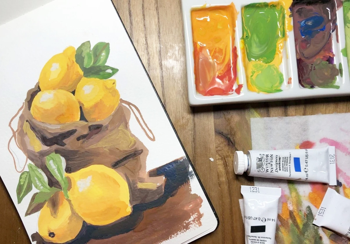 acrylic painting of lemons in brown bag on table next to paint in tray and paint tubes