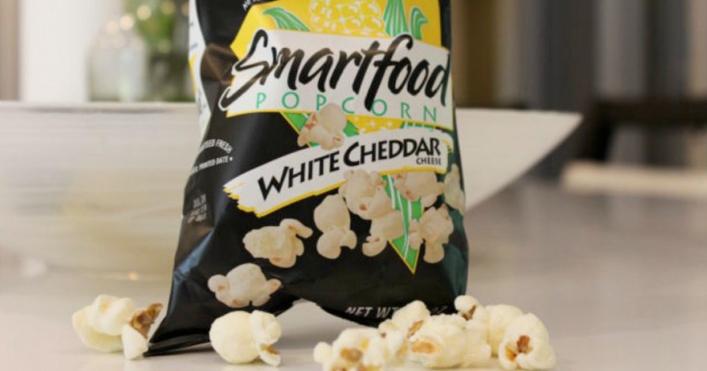 black bag of smartfood white cheddar popcorn with popcorn on table around it