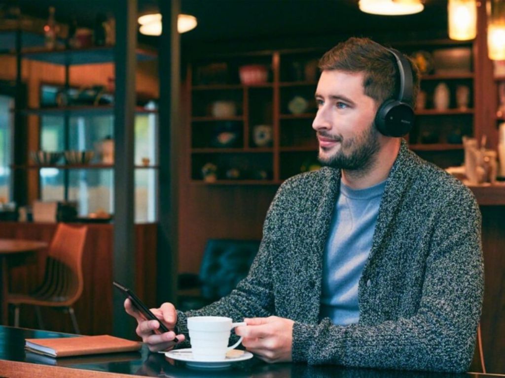 man sitting in cafe drinking coffee and wearing headphones