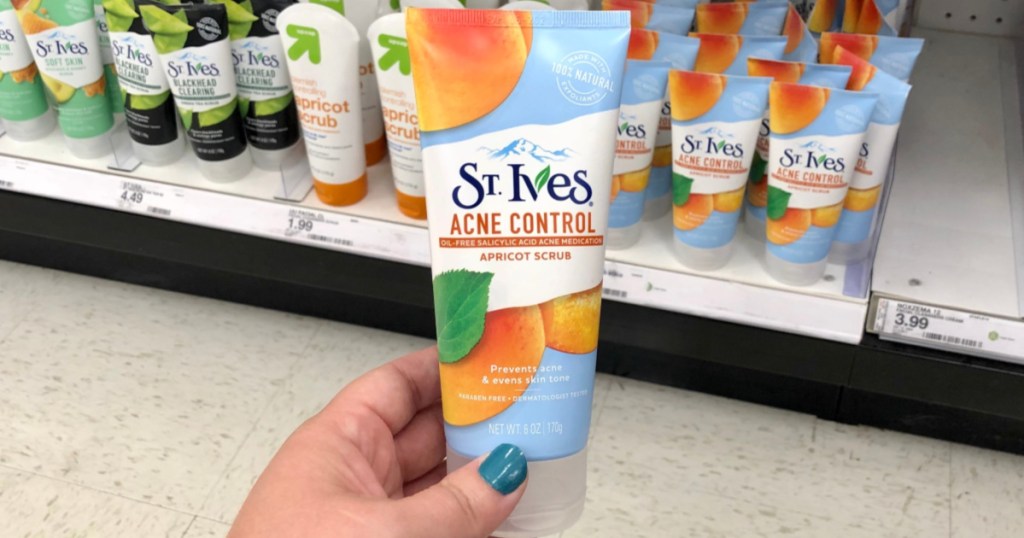manicured hand holding bottle of apricot skin scrub in store aisle
