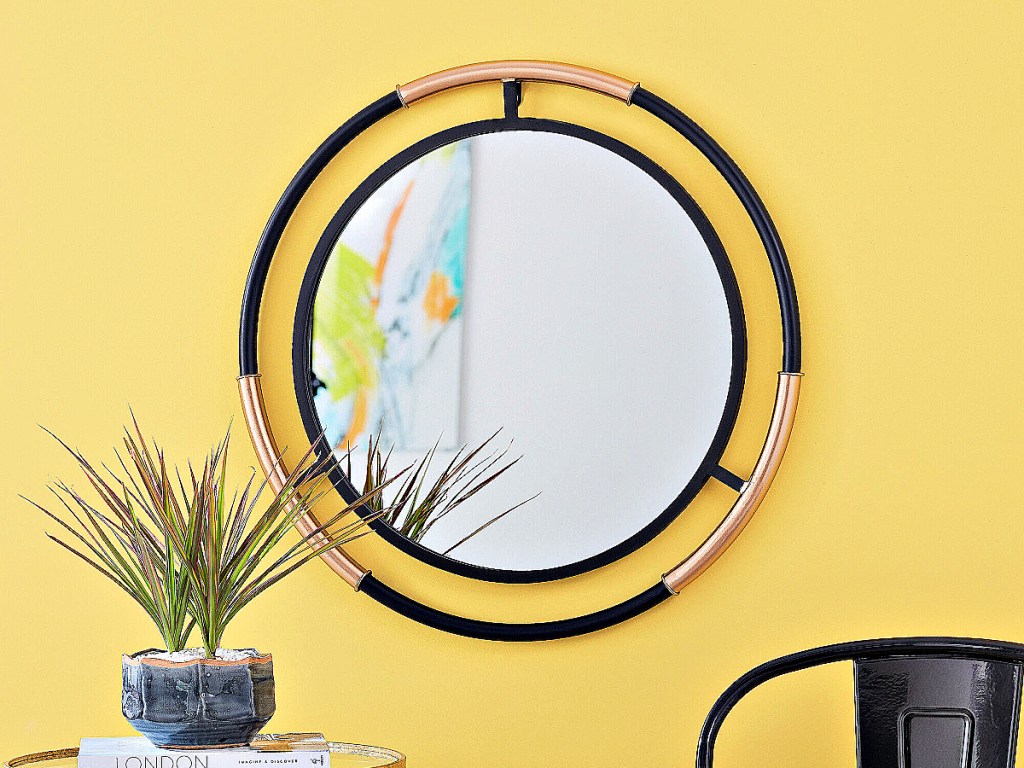 StyleWell Round Framed Blacked and Gold Accent Mirror on yellow wall with plant on table