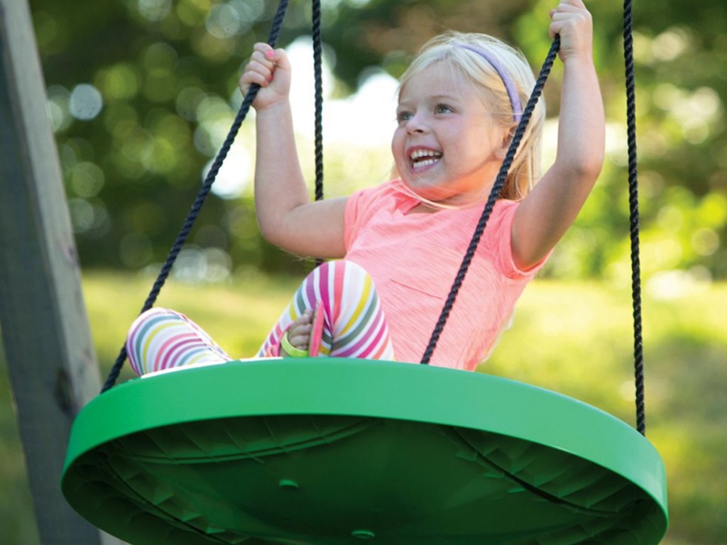 little girl sitting on a green round swing swinging and smiling