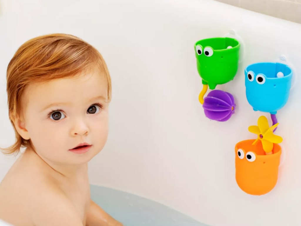 baby girl sitting in a bath tub with bath toys attached to the side of the tub