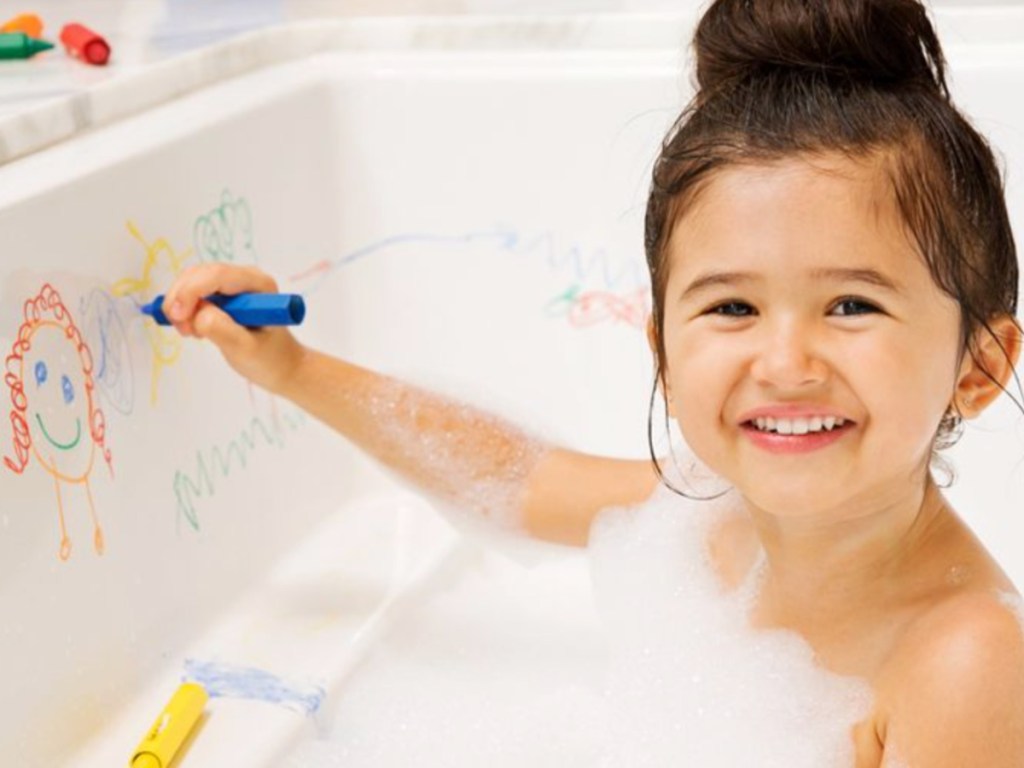 little girl sitting in a bath tub drawing on the side 