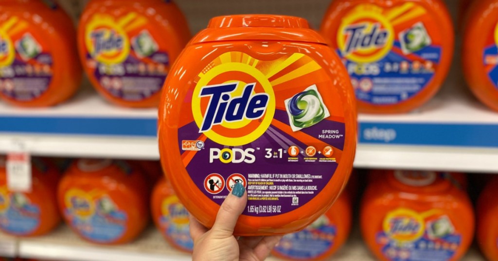 manicured hand holding tub of laundry detergent pacs in laundry aisle in store