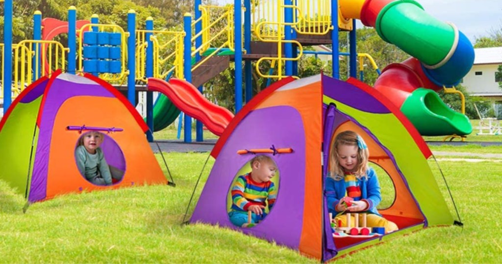 children in two colorful tents in grass by playground