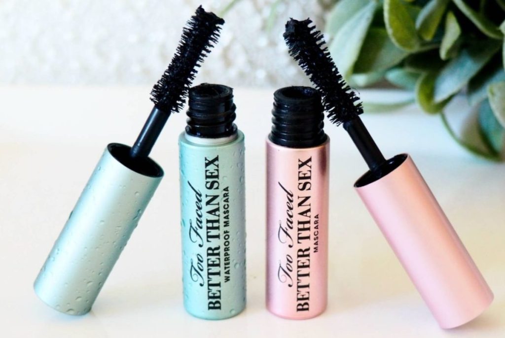 blue trial-size mascara and pink trial-size mascara tubes on white table with plant in background