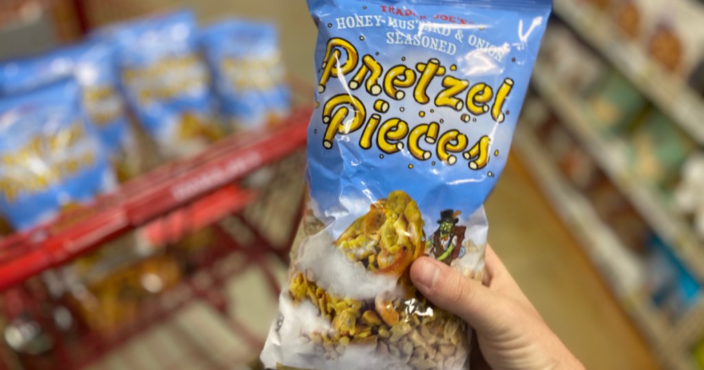 hand holding back of Trader Joe's Pretzel Pieces with multiple in cart
