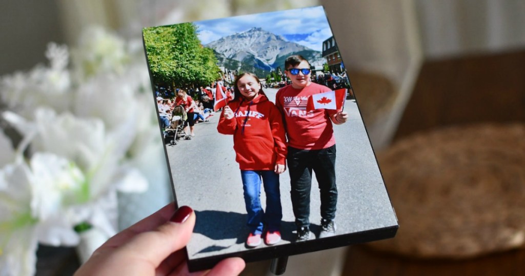 Woman's hand holding up a wooden photo panel of two kids outdoors