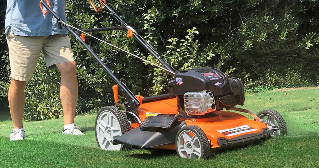 man pushing black and orange lawn mower across lawn