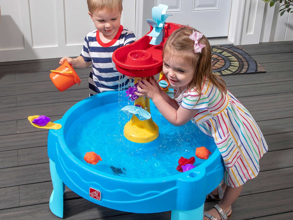 two kids playing with a water table on a porch.
