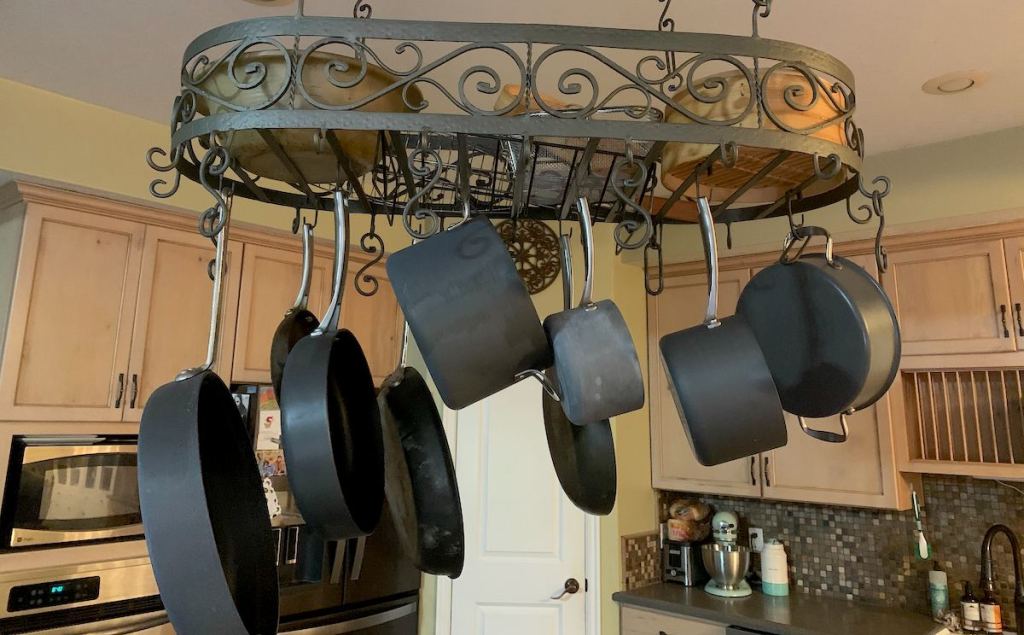 Various sizes of black pots and pans hanging from metal kitchen ceiling hanger